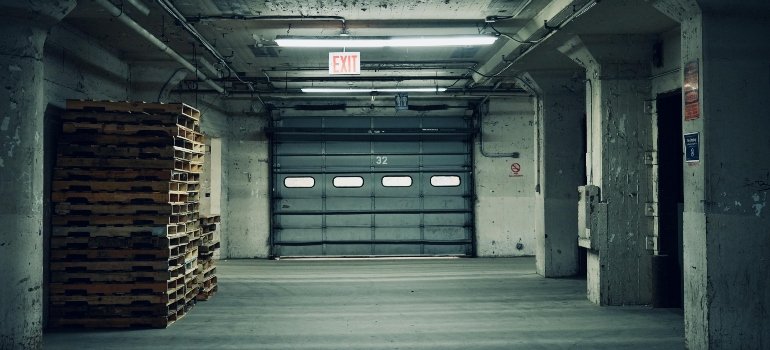 Empty industrial warehouse space with stacked wooden pallets and closed garage door.