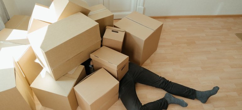 Person lying on the floor covered with cardboard boxes while strugling with balancing mental health challenges during a relocation