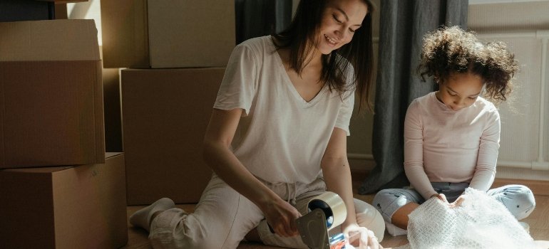 A mum and a daughter sitting on the floor with tape dispenser, talking about how to protect your belongings during renovation with temporary storage