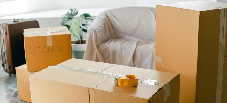 A cardboard boxes with tape on top, behind a covered sofa, to show how to protect your belongings during renovation with temporary storage