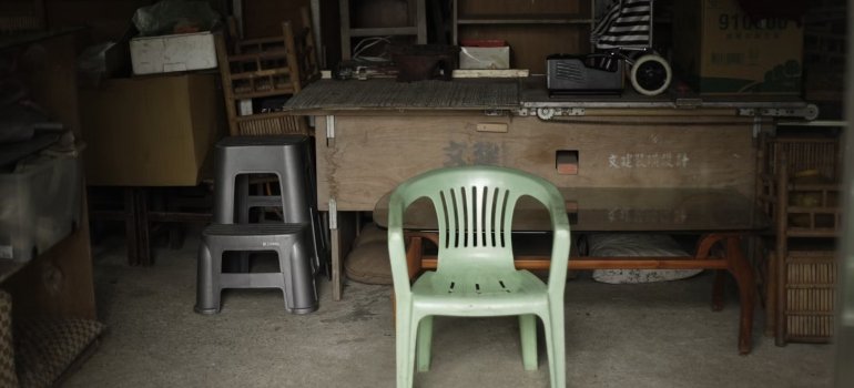A green plastic chair, two black plastic chairs and a wooden table in a storage, organization of space in a storage is the key when you pack and store large furniture