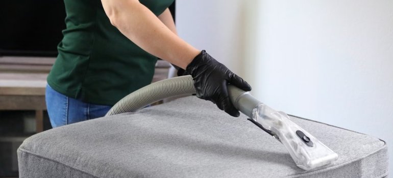 A person vacuuming a grey sofa a good tip before you pack and store large furniture