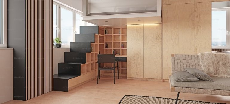 A room with a staircase, a desk, a chair and a sofa