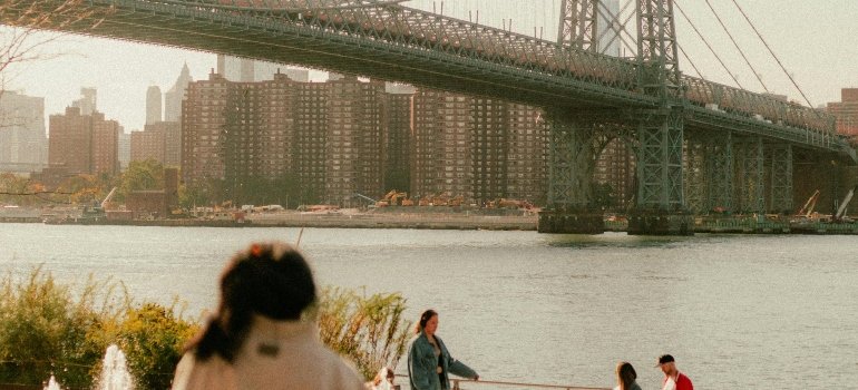 A woman is looking at the bridge near the river.