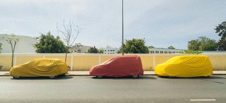 Three cars covered by colorful car covers.