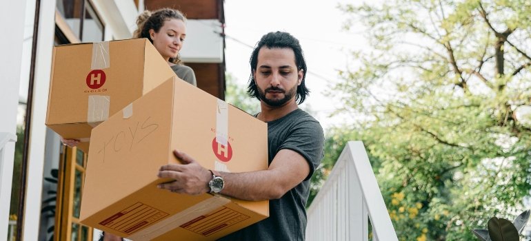 Man and woman carrying cardboard boxes while moving out of a home during a Last-Minute Summer Move in NYC.
