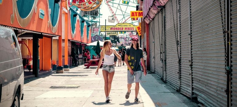 Couple walking hand-in-hand past amusement rides and food stands on a lively boardwalk.