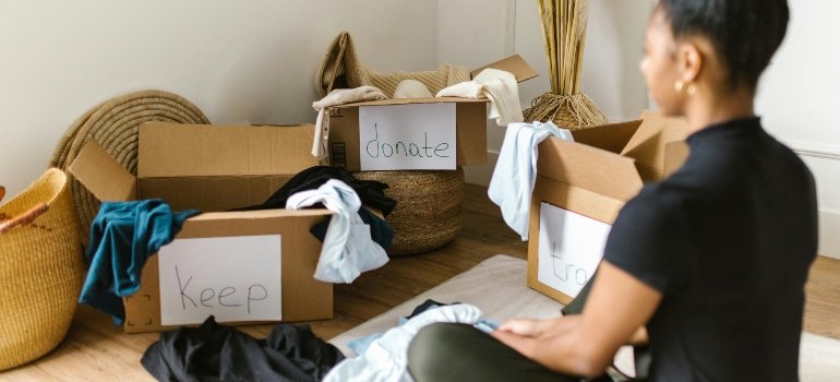 Woman sorting clothes into labeled boxes for keeping, donating, or discarding during a move.