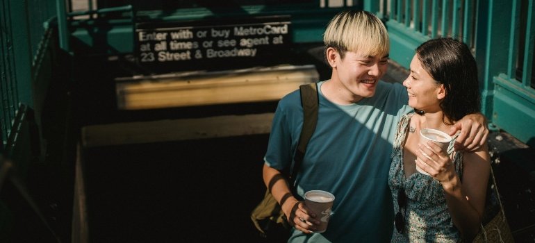 Young couple laughing while exiting a New York subway station with drinks in hand.