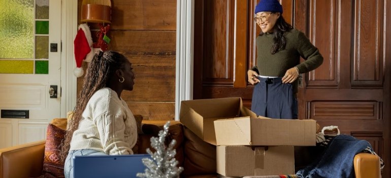 A woman standing next to a woman sitting in a room with boxes talking about NYC neighborhoods with the highest demand for storage.