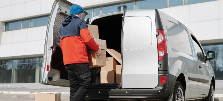 A man in a red jacket is carrying a box in the van.