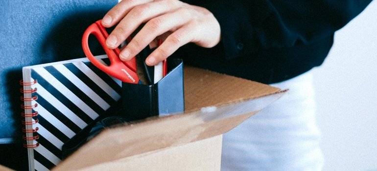 A person is holding office supplies in a box.