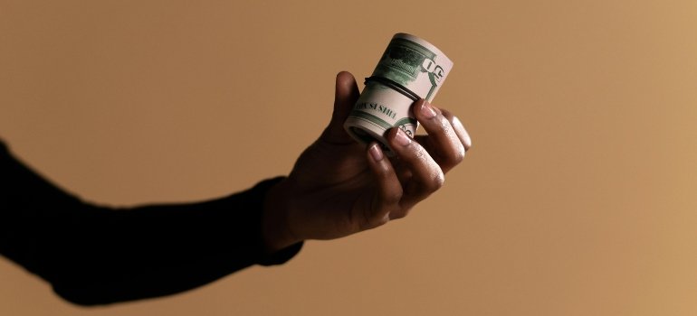 A hand holding a roll of US currency — perfect visual metaphor for saving money with an Unusually Cheap Storage Unit in Manhattan.