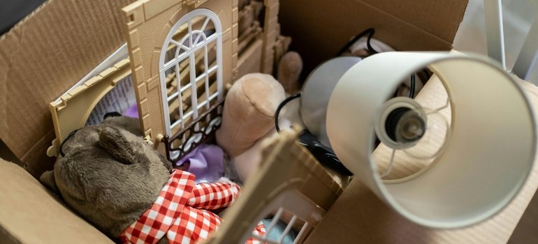 A cardboard box filled with toys and a lamp shade, showing practical attic storage ideas for organizing household items.