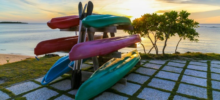 Rack with colorful kayaks near the ocean, illustrating Storing Summer Equipment Safely.