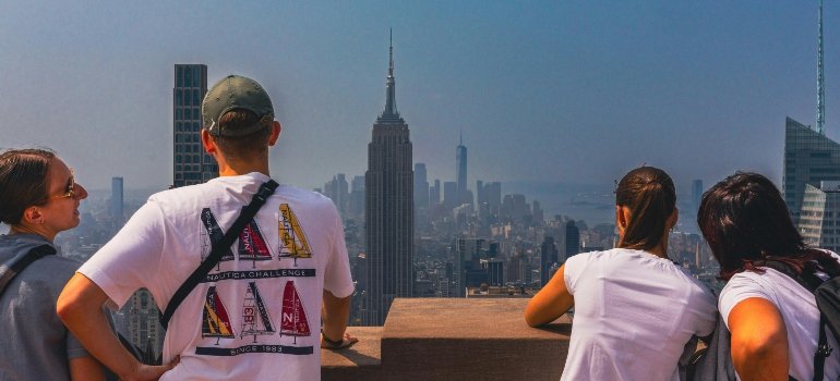 Tourists leaning over a ledge, staring at the Empire State Building and the cityscape.