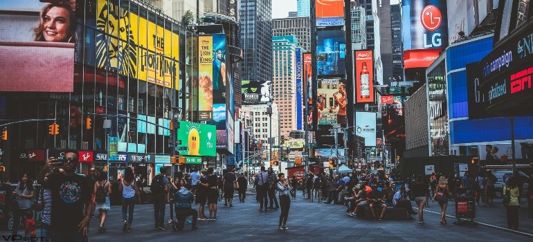 Daytime Times Square with people walking and giant ads towering above facing the Myths About Moving to Manhattan.