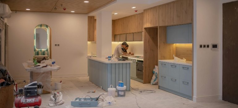 A couple renovating their kitchen while discussing repairs before renting out their Bronx apartment.