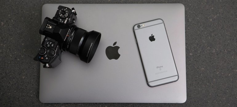 A MacBook, iPhone, and professional camera arranged on a gray surface for secure storage.