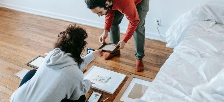 A couple arranging framed pictures on the floor before decorating their new apartment.