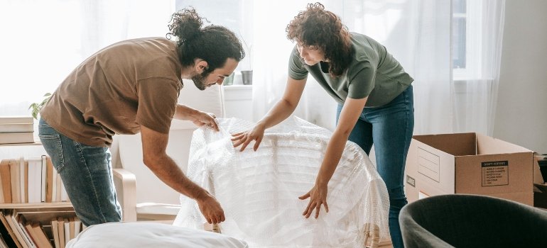 Couple wrapping a chair in bubble wrap to prioritize safety during a last-minute relocation in NYC.