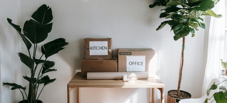 Cardboard boxes labeled kitchen and office placed on a wooden table ready for storage.