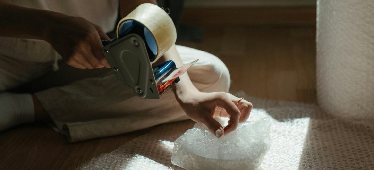 Close-up of hands carefully wrapping a dish in bubble wrap for protection.