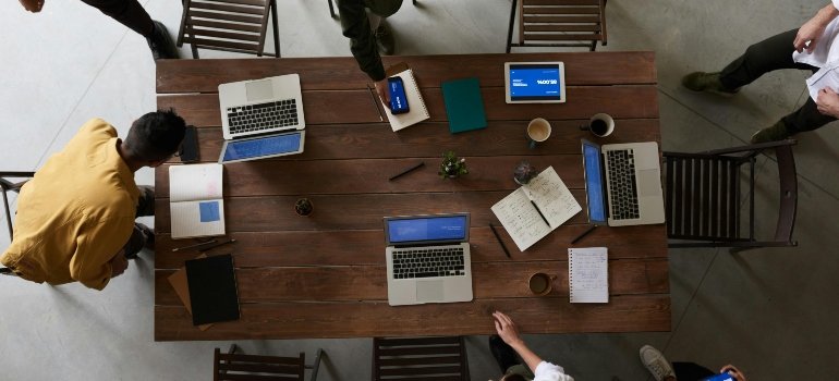 Group of professionals with laptops gathered at table discussing office storage planning.