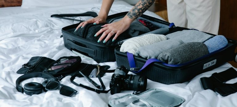Hands pushing clothes into a suitcase.