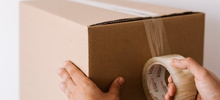 A person sealing a moving box