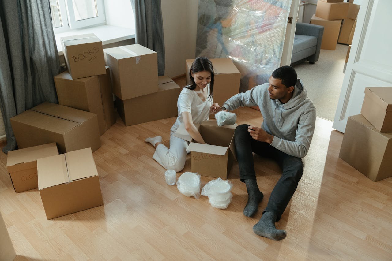 A young couple sitting on the floor, packing boxes.