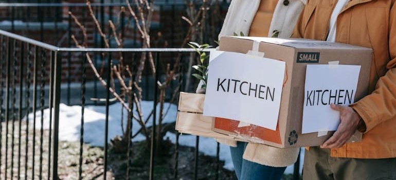 A person carrying a moving box labeled kitchen