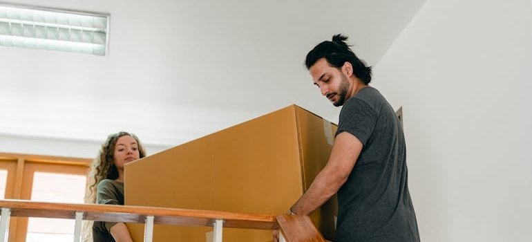 A couple relocating a moving box by using a box size guide for NYC moves