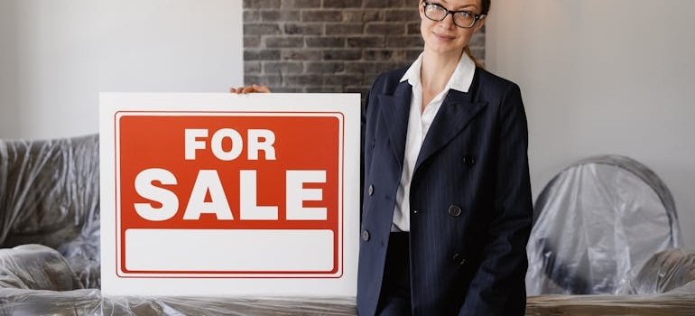 A woman standing next to the for sale sign