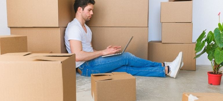 A man sitting next to the boxes and using laptop